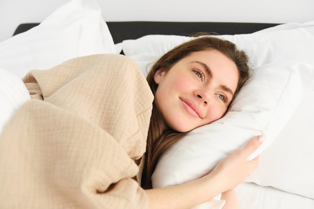 Kostenloses Foto wunderschöne frau, die im schlafanzug im bett liegt, ihr kissen umarmt und lächelt