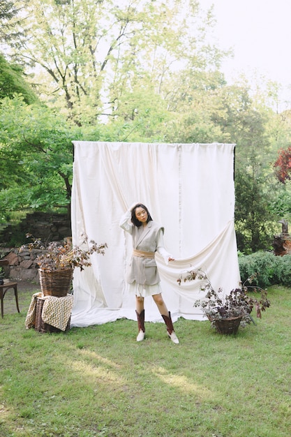 Wunderschöne Frau im weißen und grauen Kleid, die auf dem Boden sitzt und im Garten schaut.