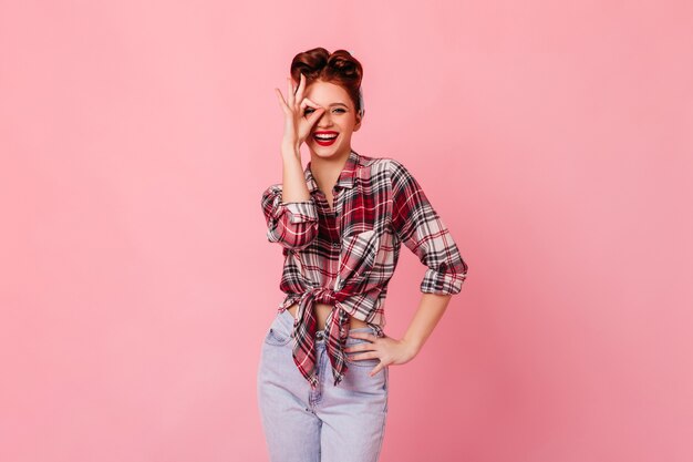 Wunderschöne Frau in Jeans, die okay Zeichen zeigt. Lachendes Pinup-Mädchen, das auf rosa Raum gestikuliert.