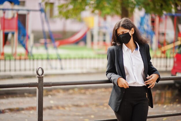 Wunderschöne indische Frau trägt eine formelle und schwarze Gesichtsmaske, die während der Covid-Pandemie auf der Straße posiert