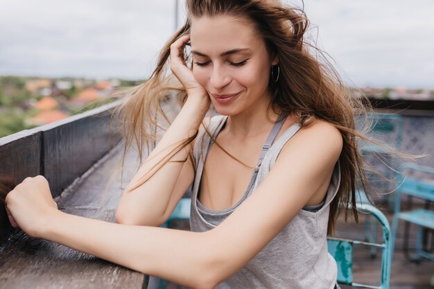 Wunderschöne junge Frau verträumt posiert im Frühlingswochenende. Attraktives weibliches Modell mit langen dunklen Haaren, die mit geschlossenen Augen am Dach sitzen.