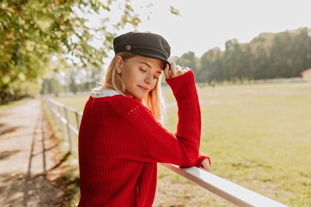 Wunderschönes blondes Modell, das sich im sonnigen Herbstwetter ruhig fühlt. Junge Frau, die trendigen Hut mit netten Accessoires trägt.