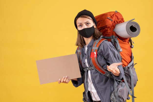 wunderte sich reisendes Mädchen mit schwarzer Maske und Rucksack mit Karton