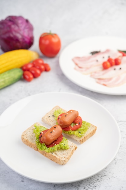 Wurst mit Tomaten, Salat und zwei Sätzen Brot auf einem weißen Teller.