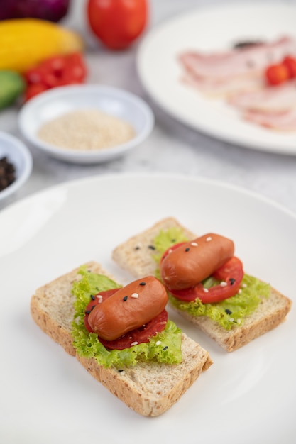 Wurst mit Tomaten, Salat und zwei Sätzen Brot auf einem weißen Teller.