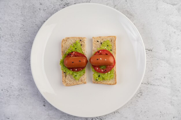 Wurst mit Tomaten, Salat und zwei Sätzen Brot auf einem weißen Teller.