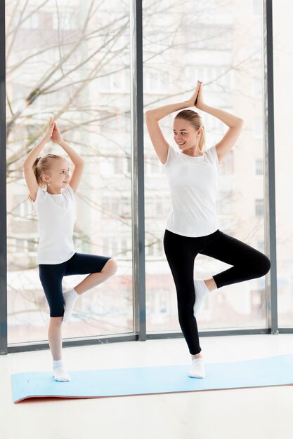 Yoga-Pose mit Mutter und Smiley-Tochter zu Hause