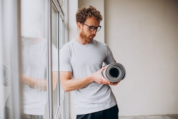 Yogatrainer mit Matte am Fenster stehend