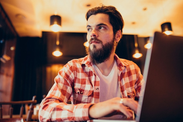 Youn g bärtiger Mann, der an Laptop in einer Stange arbeitet