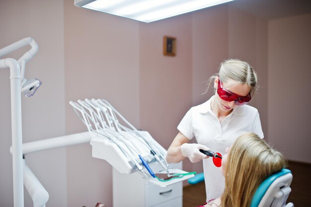 Zahnärztin in einer speziellen roten Brille, die die Zähne ihrer Patientin mit zahnärztlichen Instrumenten behandelt