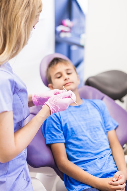 Zahnarzt, der nahe dem Jungen den Skalator sitzt auf zahnmedizinischem Stuhl hält