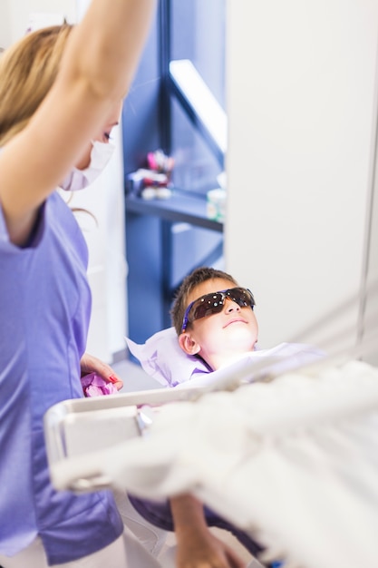 Zahnarzt, der Schutzbrillen des Jungen tragende Sicherheit betrachtet