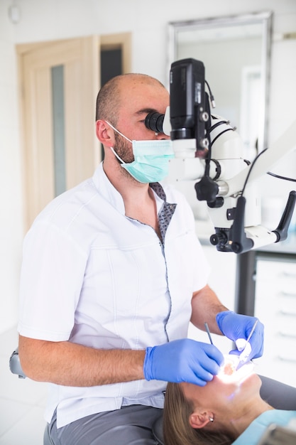 Zahnarzt, der zahnmedizinisches Mikroskop für das Behandeln der Zähne des weiblichen Patienten verwendet