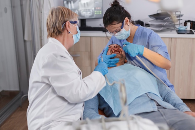 Zahnarztgruppe von Ärzten mit medizinischen Gesichtsmasken mit professionellen zahnärztlichen Werkzeugen während der stomatologischen Chirurgie im Büroraum des zahnärztlichen Krankenhauses. Kieferorthopäde, der bei der Gesundheitsbehandlung arbeitet