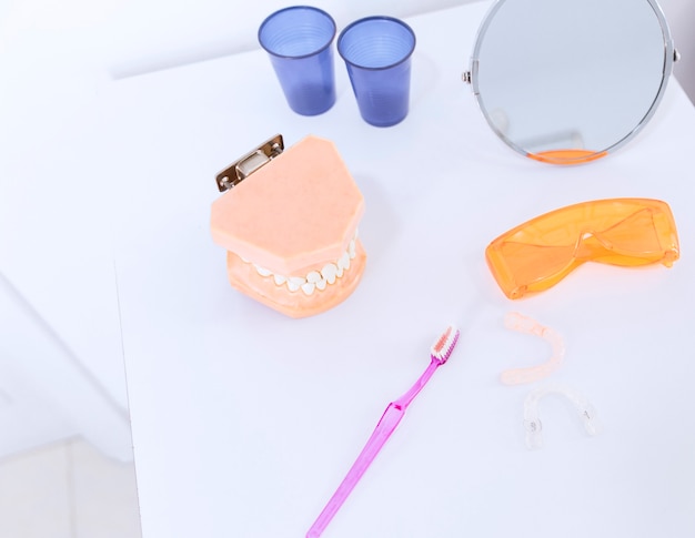 Zahnprothese; Schutzbrille; Zahnbürste; Spiegel und Zahnausrichter auf dem Tisch