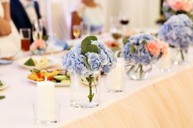 Zarte Blumensträuße von blauen Hortensien stehen in den Gläsern auf Abendtisch