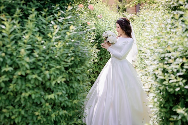 Zarte brünette Braut steht im grünen Garten und schnüffelt Hochzeitsstraußduft