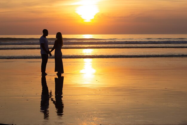 Zarte Familie, die bei Sonnenuntergang am Strand spazieren geht. Mann und Frau in Freizeitkleidung, die in der Abenddämmerung am Wasser spazieren. Liebe, Familie, Naturkonzept