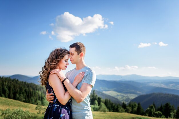Zarte Umarmungen eines Paares, das auf einem grünen Hügel vor herrlicher Landschaft steht