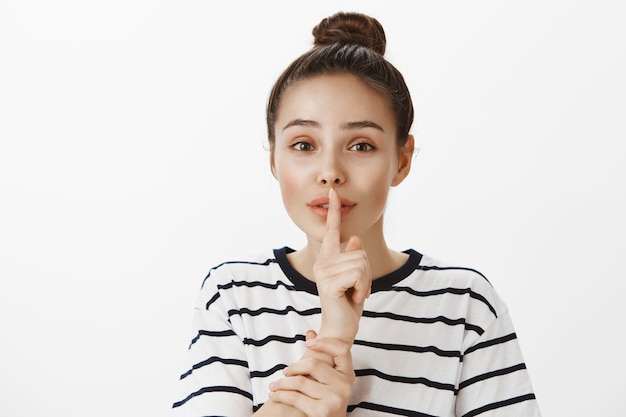 Zartes attraktives Mädchen, das Geheimnis erzählt, Schweigen, Schweigengeste mit Finger über Lippen macht