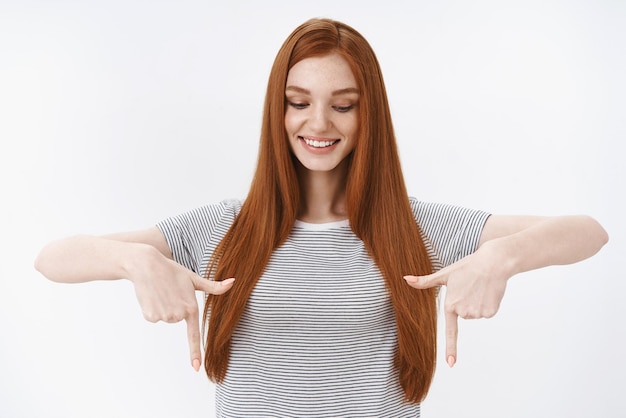 Kostenloses Foto zartes, feminines, enthusiastisches, fasziniertes, rothaariges mädchen, langes glattes haar, das amüsiert nach unten zeigende zeigefinger zeigt, die daran interessiert sind, erstaunliche landschaften zu beobachten, die den berg genießen und die landschaft genießen