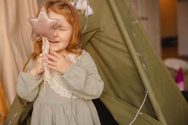 Zartes rothaariges kleines kaukasisches Mädchen mit geschlossenen Augen trägt drinnen Kleid Kinder-Lifestyle-Konzept