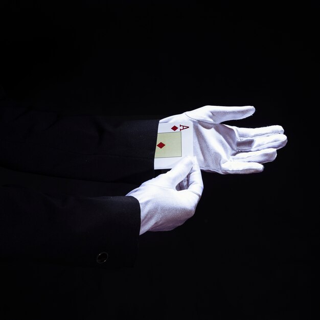 Zauberer, der Spielkarte der Asse von der Hand gegen schwarzen Hintergrund entfernt