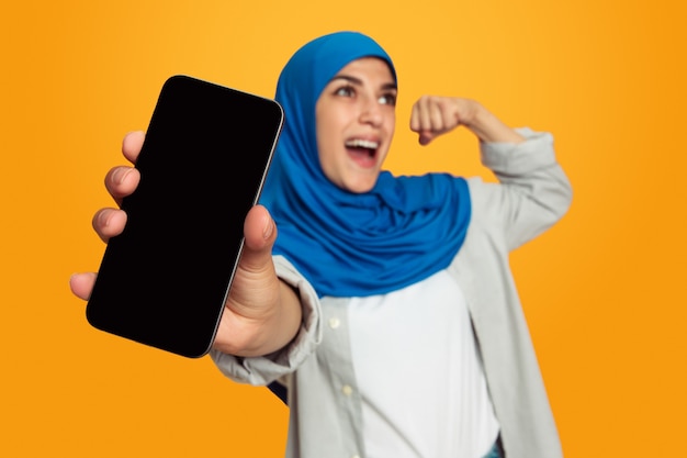 Zeigt leeren Telefonbildschirm Junge muslimische Frau isoliert auf gelber Wand