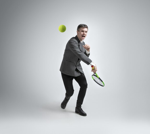 Zeit für Bewegung. Mann in Bürokleidung spielt Tennis isoliert auf grauem Hintergrund