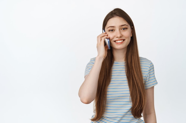 Zellulares und mobiles Konzept. Junge Frau, die am Telefon spricht, einen Anruf tätigt und glücklich lächelt, stehend auf Weiß.