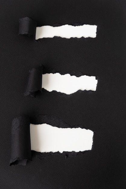 Zerrissenes schwarzes Papier, das Weiß aufdeckt