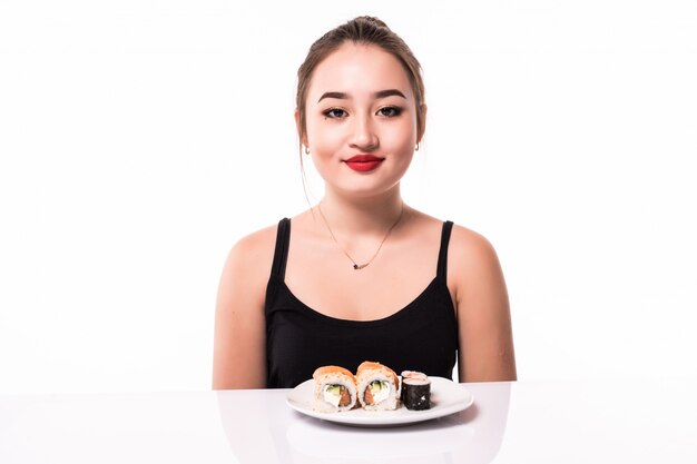 Ziemlich asiatischer Blick mit bescheidener Frisur sitzen auf dem Tisch essen Sushi-Rollen lächelnd isoliert auf Weiß