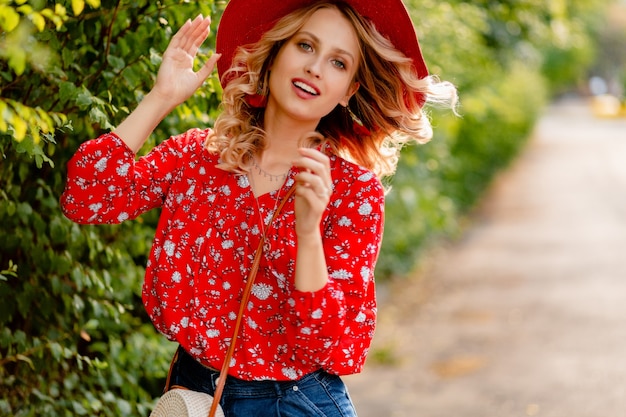 Ziemlich attraktive stilvolle blonde lächelnde Frau in strohrotem Hut und Bluse Sommermode-Outfit