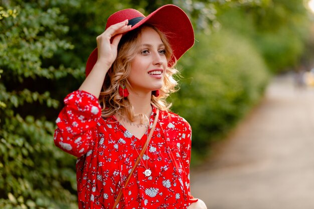 Ziemlich attraktive stilvolle blonde lächelnde Frau in strohrotem Hut und Bluse Sommermode-Outfit