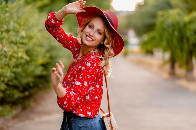 Ziemlich attraktive stilvolle blonde lächelnde Frau in strohrotem Hut und Bluse Sommermode-Outfit