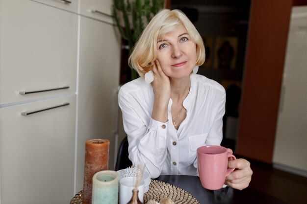 Ziemlich schlanke reife blonde Frau, die Morgen mit Kaffee genießt