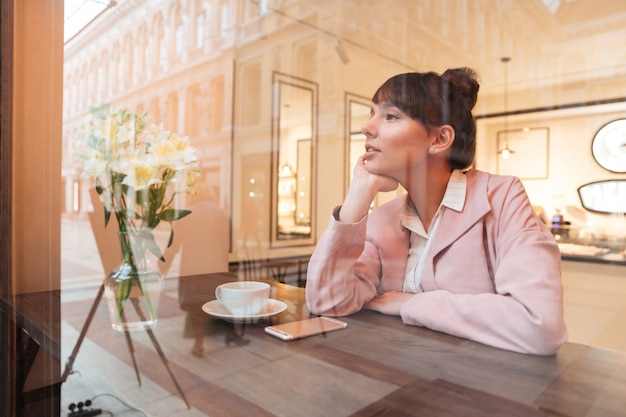 Ziemlich träumende junge Frau, die am Kaffeetisch sitzt