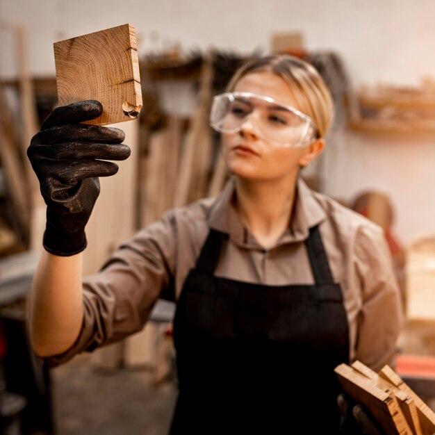 Zimmermannin mit Brille, die ein Stück Holz betrachtet