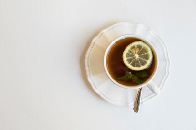 Zitronen-Minz-Teetasse; Löffel auf keramischer Untertasse über weißem Hintergrund
