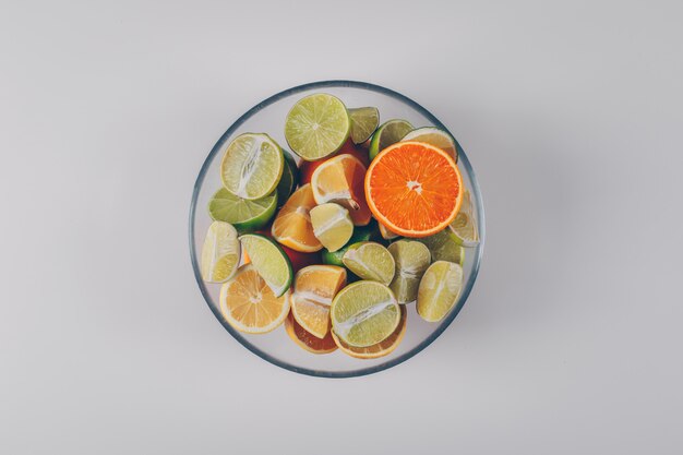 Zitronen mit grünen Zitronen und Orange in einer Schüssel auf weißem Hintergrund, Draufsicht.