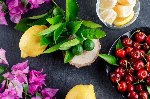 Zitronen mit Scheiben, Blättern, Blumen, Kirschen, Holzbrett auf grauer Oberfläche, Draufsicht