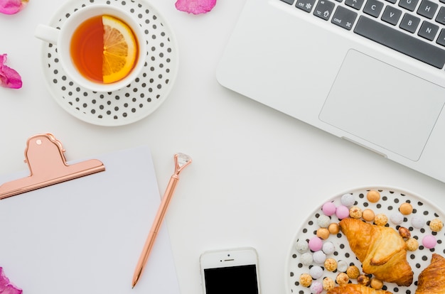 Zitronenteetasse; Laptop; Croissant; Süßigkeiten; Mobiltelefon; Stift und Zwischenablage auf weißem Hintergrund