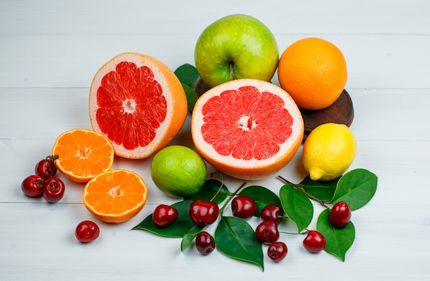 Zitrusfrüchte mit Apfel, Kirschen, Blättern liegen flach auf einem Holztisch