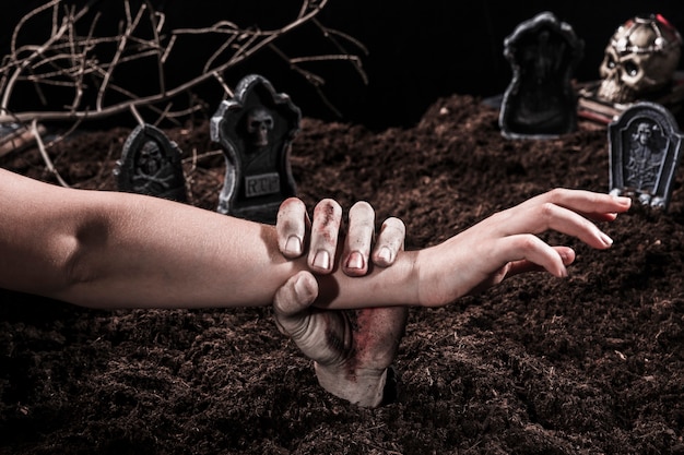 Zombiehand, die Personenarm an Halloween-Friedhof hält