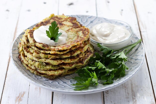 Zucchini-Krapfen mit Joghurtsauce auf weißem Holztisch