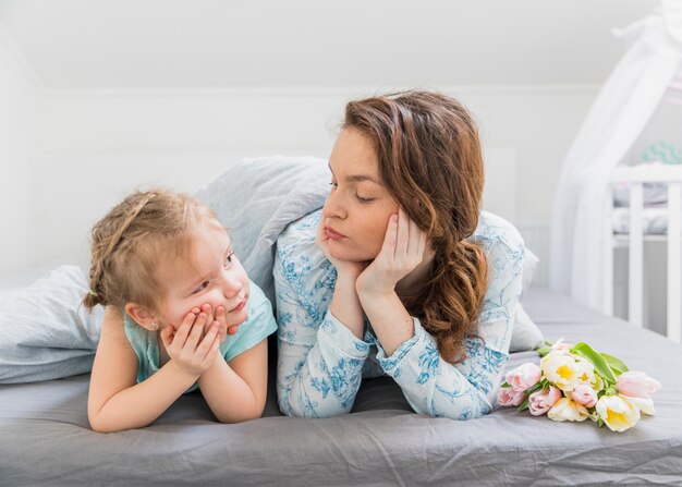 Zuckende Mutter und Tochter beim einander zu Hause betrachten im Bett