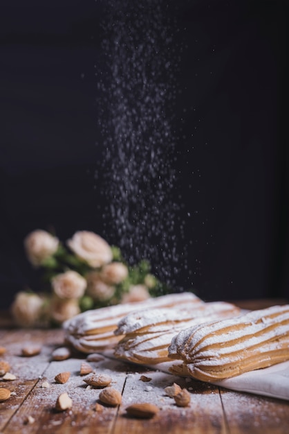 Zuckerpulver, das auf dem gebackenen Eclair mit Mandeln gegen schwarzen Hintergrund abwischt