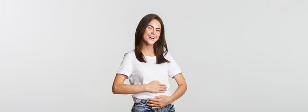 Zufrieden lächelndes brünettes Mädchen, das Bauch nach dem Essen des köstlichen Essens reibt