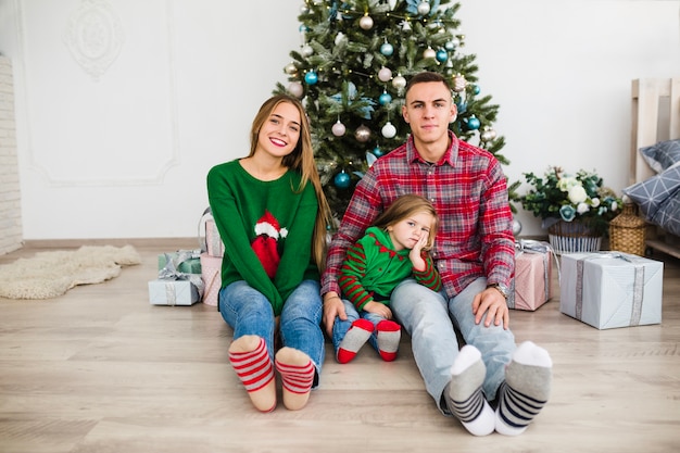 Zufriedene Familie, die vor Weihnachtsbaum sitzt