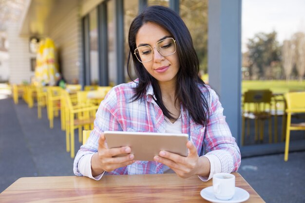 Zufriedene Frau, die Tablette verwendet und Kaffee im Café trinkt